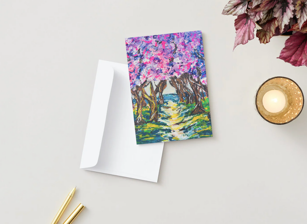 A6 greeting card featuring a vibrant, hand-painted cherry blossom tree path with a white envelope on a desk.