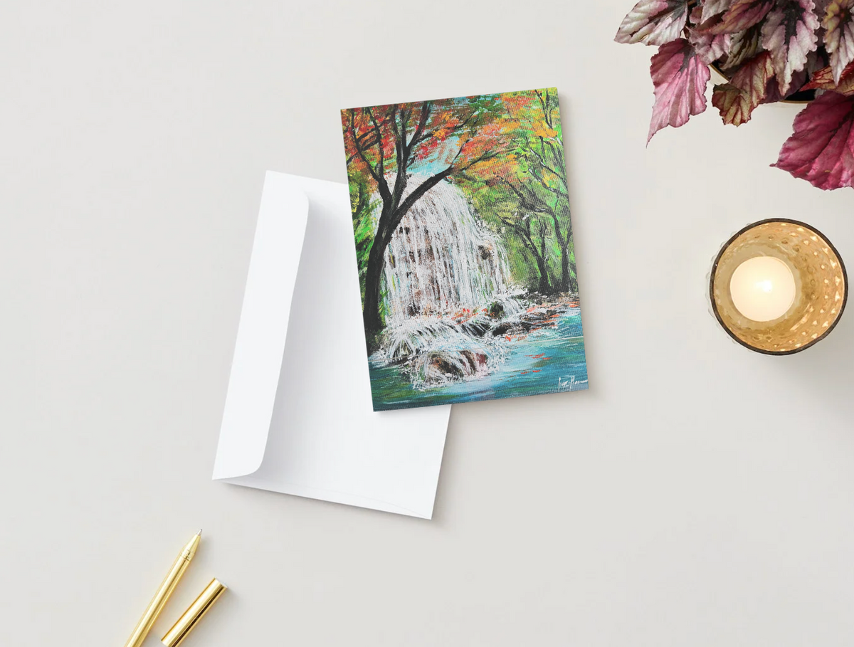 A6 greeting card featuring a waterfall painting with a white envelope on a desk with a candle and plant.