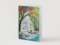 A6 greeting card featuring a hand-painted waterfall in a vibrant autumn forest with a premium satin finish.