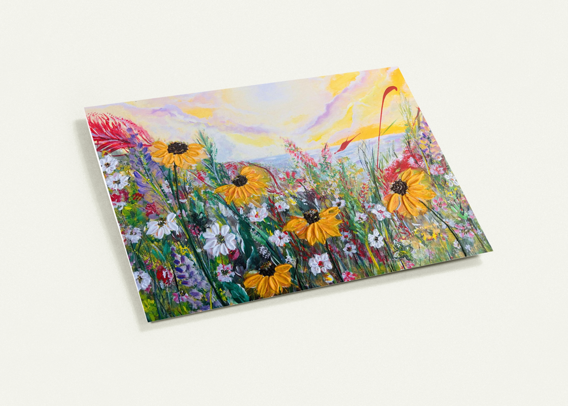 A6 horizontal greeting card featuring a vibrant, hand-painted wildflower meadow with yellow daisies and a coastal sunset.