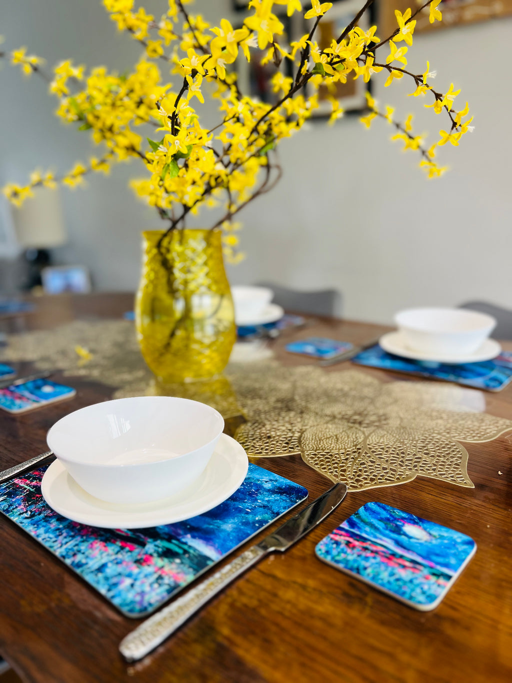 Set of four 23x19cm wooden placemats with glossy blue night sky art, displayed on a dining table with matching coasters.