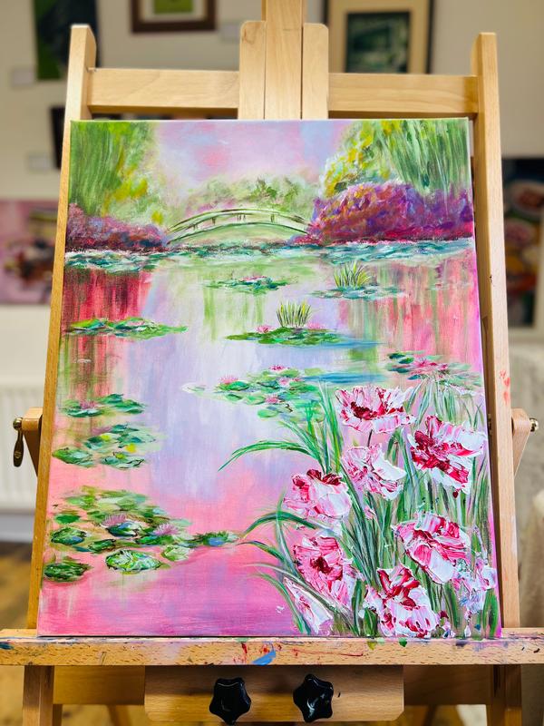 Framed artwork on an easel showing a lily pond with an arched bridge and blossoms