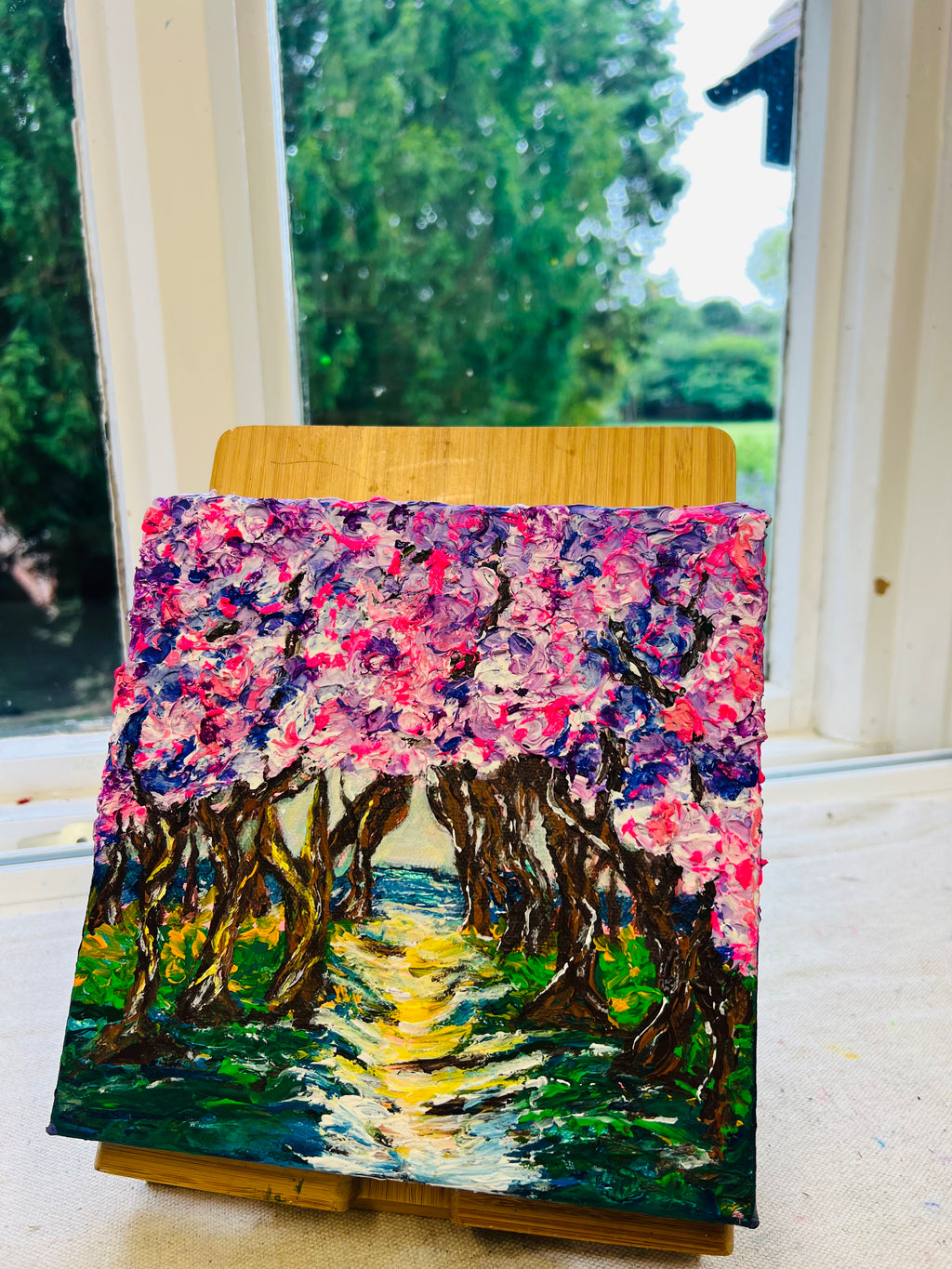 Framed 3D texture artwork on easel with bright pink sky, blue water, and green ground