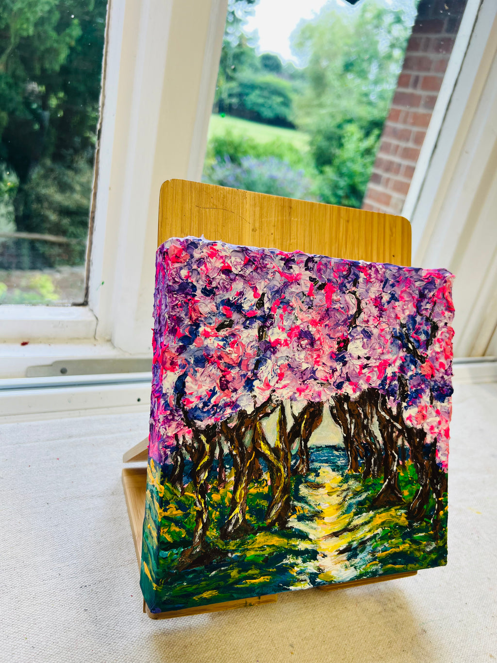 Framed 3D artwork on easel with colorful arched trees and pink textured sky