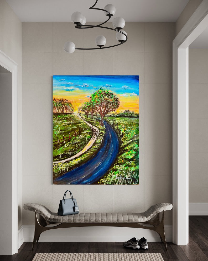 Framed landscape painting featuring a curved road, green fields, and bright sunset colors.