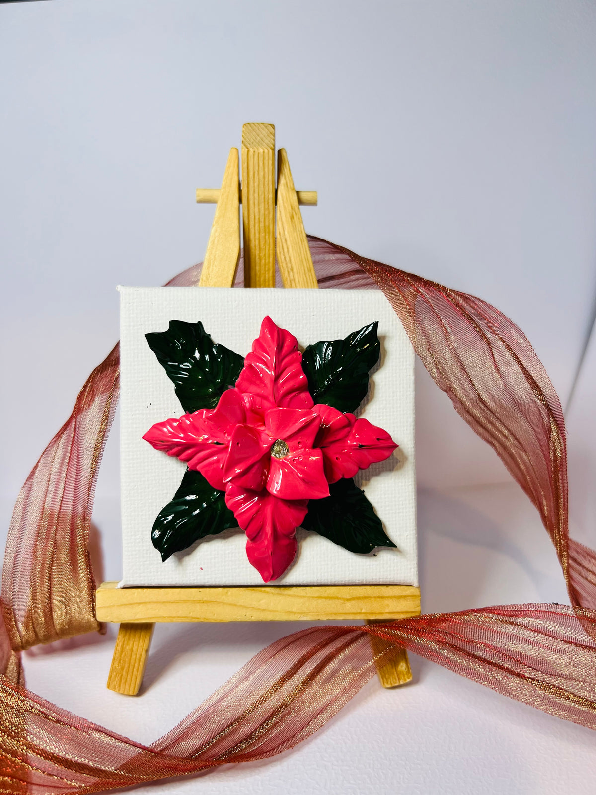 Textured 3D red poinsettia art on a 7x7cm cotton canvas displayed on a small wooden easel with decorative ribbon.