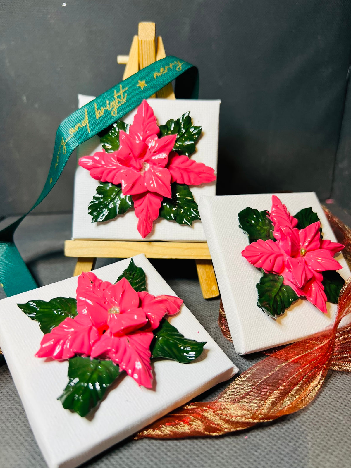 Textured pink poinsettia flowers on 7x7cm mini canvases displayed on small wooden easels with festive green ribbon.