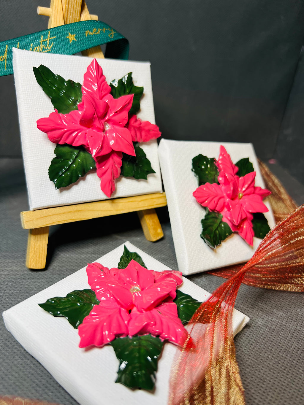 Textured pink poinsettia art on 7x7cm mini canvas and wooden easel with green and gold ribbon accents.