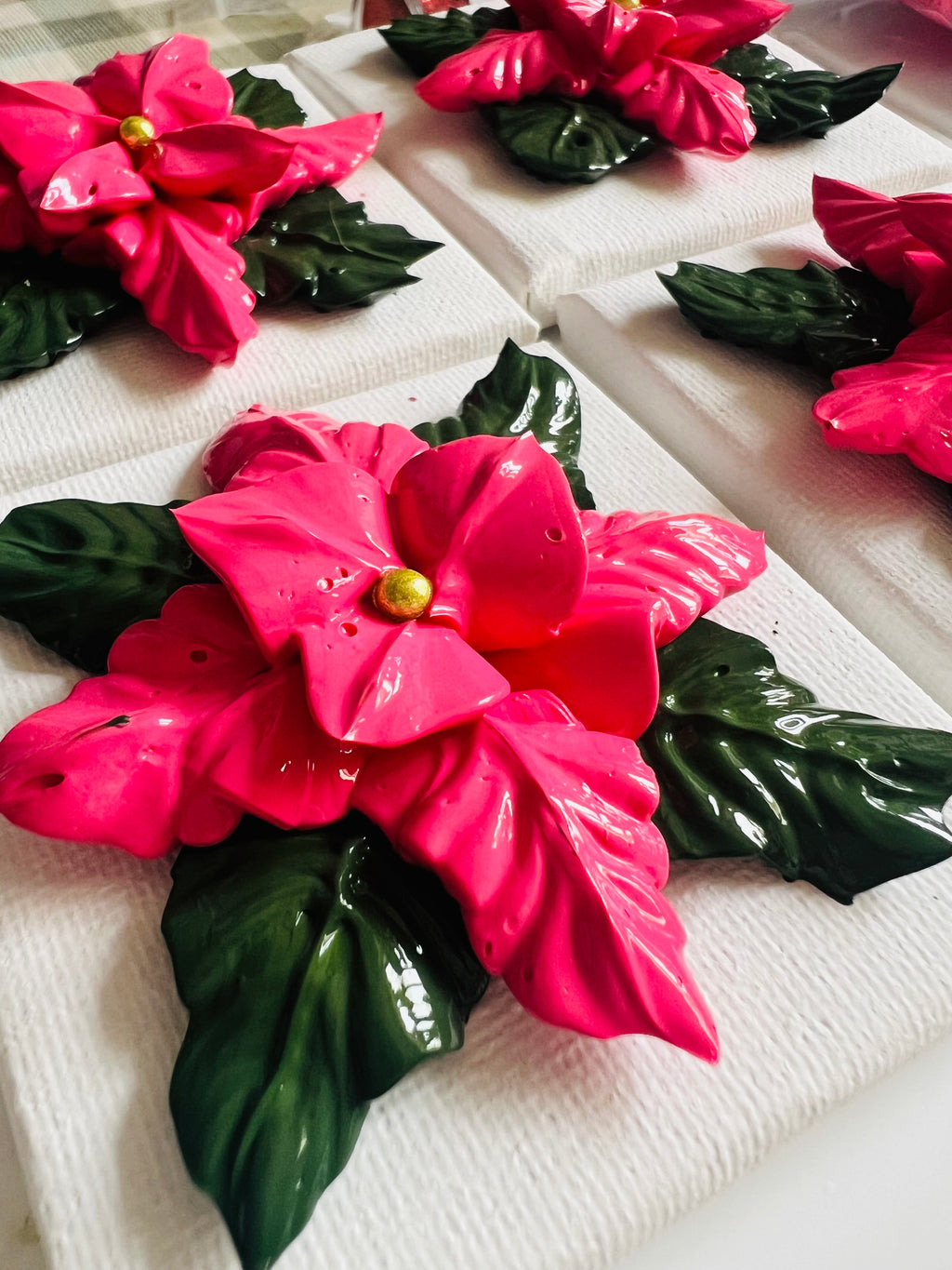Textured pink poinsettia art on 7x7cm white cotton canvas with glossy green leaves and a gold center.