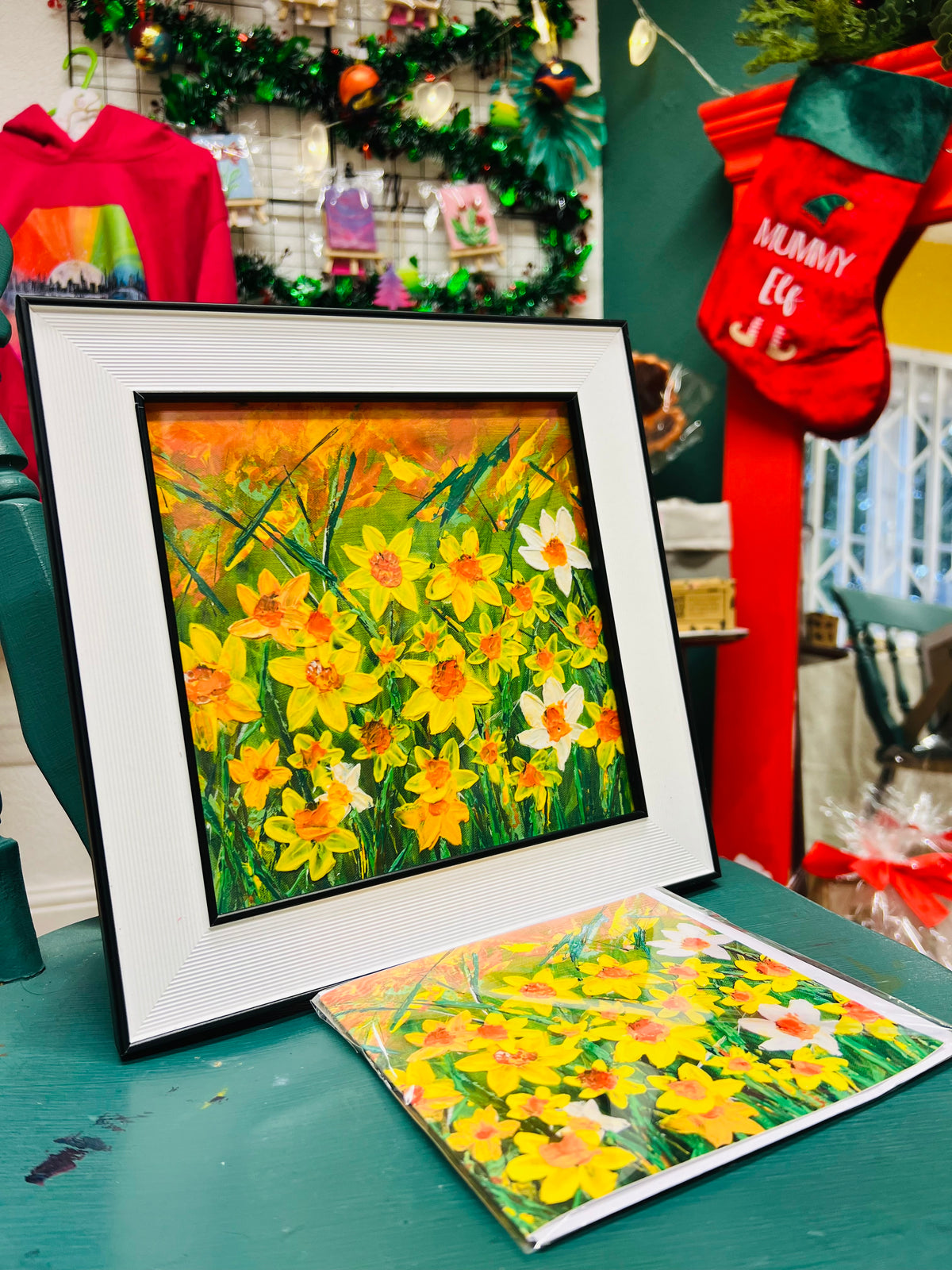 Daffodils gift set with a 10x10 inch framed floral art print and a matching fine art card on a green surface.