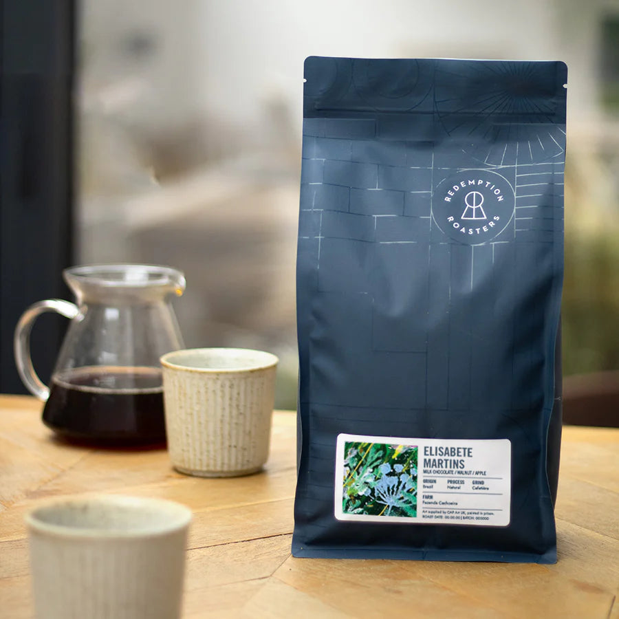 Dark blue coffee bag with ELISABETE MARTINS label near mug and coffee pot