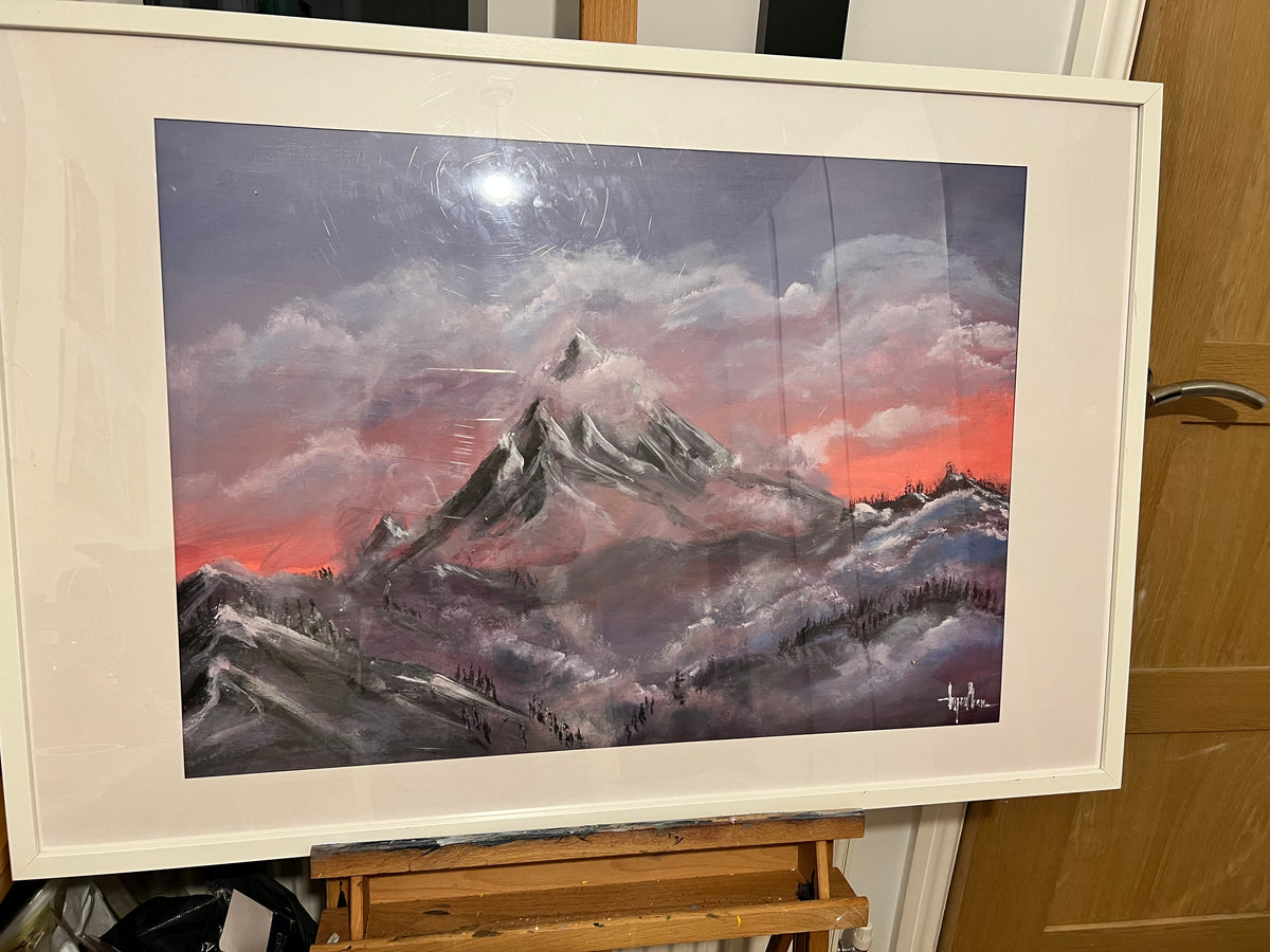 Mountain sunrise painting in a white frame, snowy peaks, and glowing cloudy sky