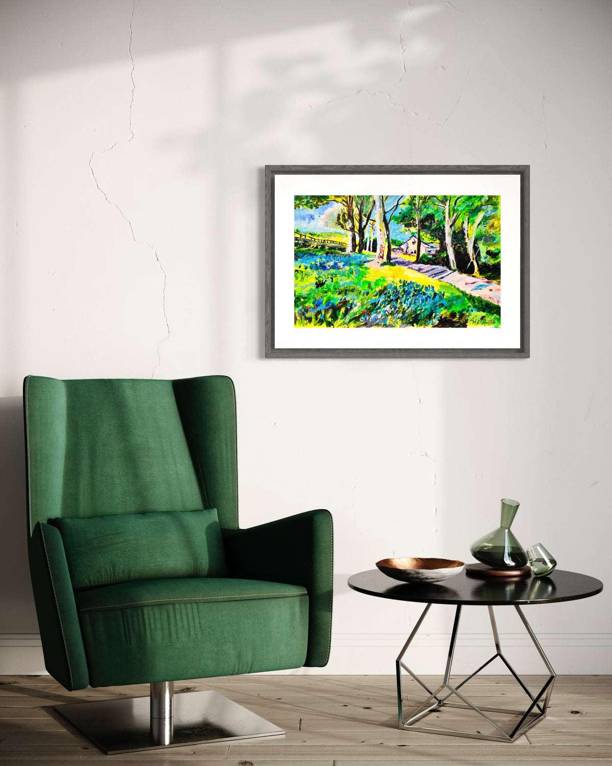 Framed watercolor landscape painting with bluebell field, trees, and path on a wall