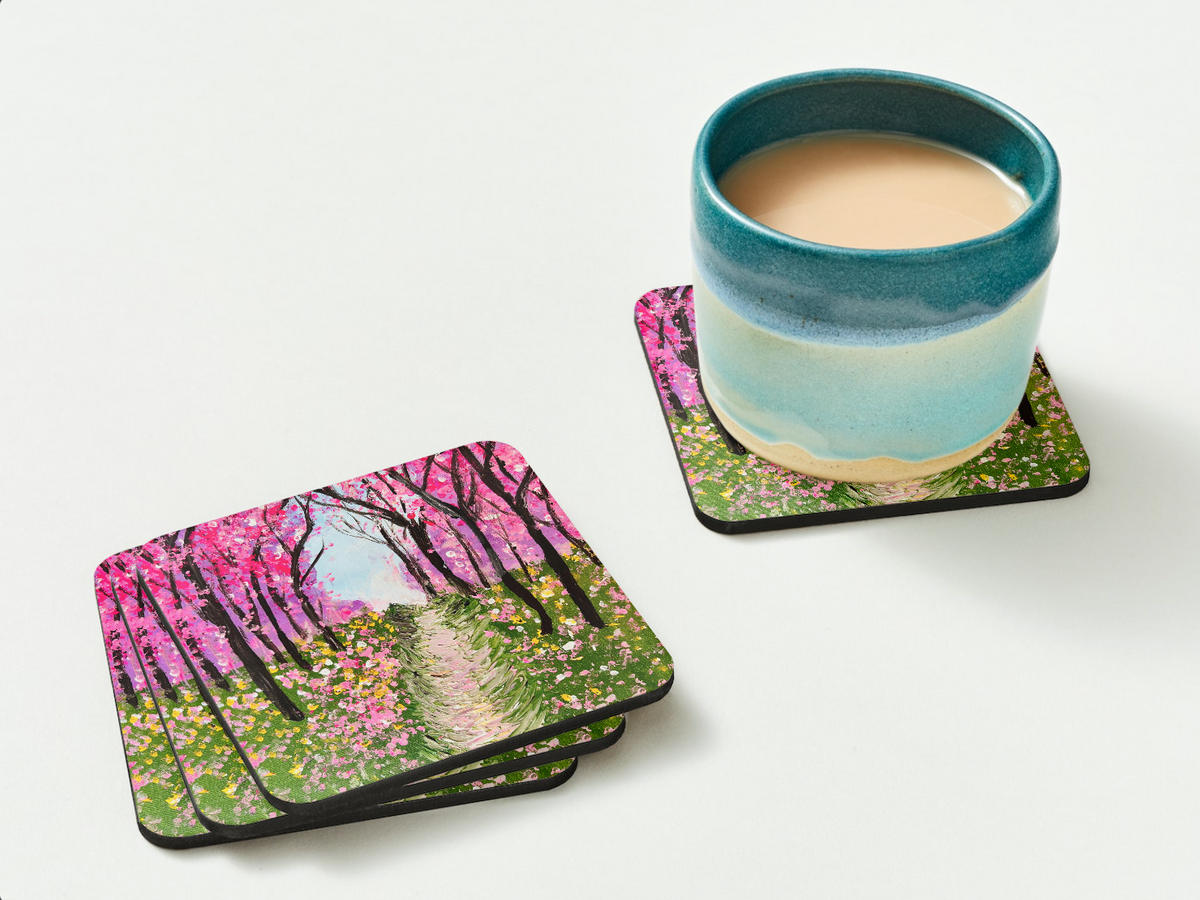 Glossy 9.5cm hardboard coaster featuring a pink cherry tree walkway painting, shown with a ceramic mug on a white surface.