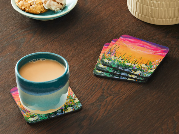Glossy 9.5cm hardboard coasters featuring a vibrant, colourful floral field acrylic painting design on a wooden table.