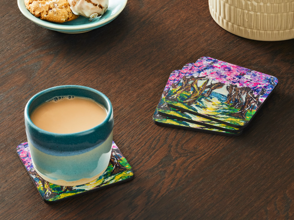 Glossy 9.5cm hardboard coaster featuring a vibrant pink and purple floral acrylic painting on a wooden table.