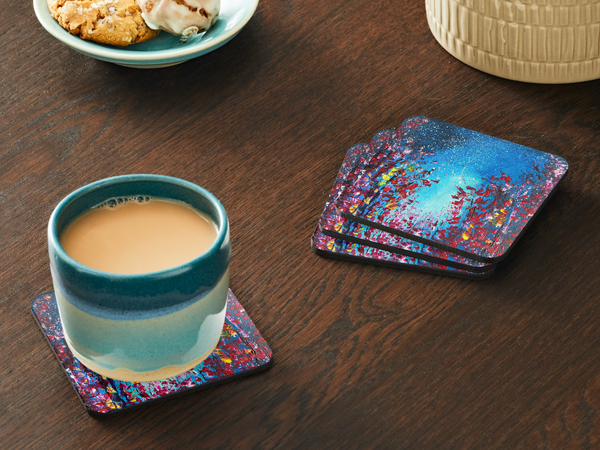 Square 9.5cm hardboard coasters with a glossy dark blue starry night and floral acrylic art print on a wooden table.