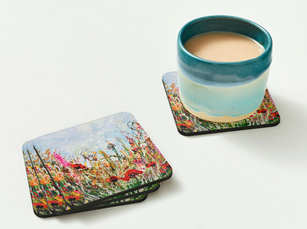 Glossy 9.5cm hardboard coaster featuring a vibrant wildflower meadow painting, shown with a blue ceramic mug on a white surface.