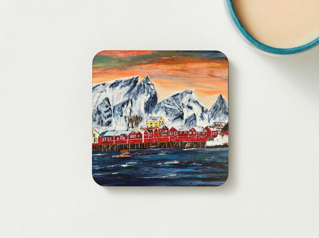 Hardboard coaster close-up with fishing village artwork: snowy peaks, red houses, blue sea.
