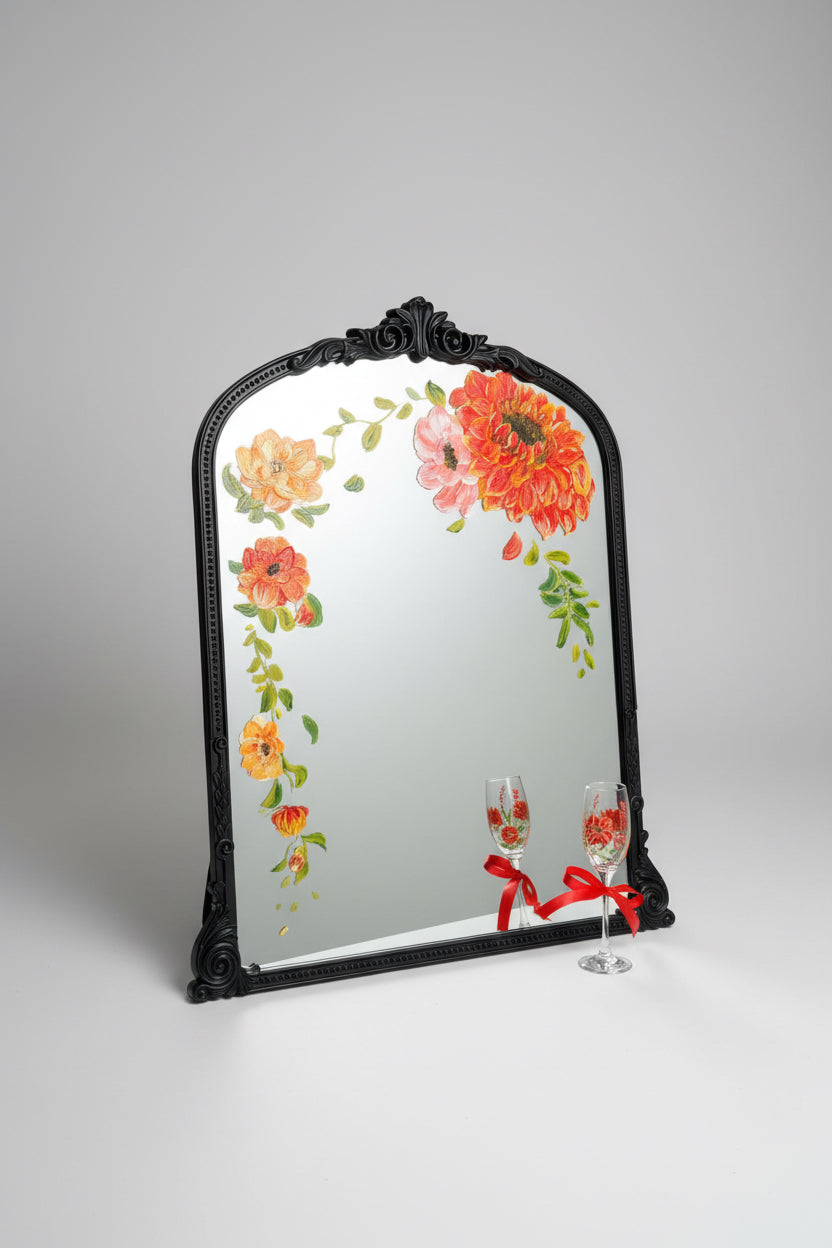 Decorative mirror with floral design and matching glasses on a wooden surface.