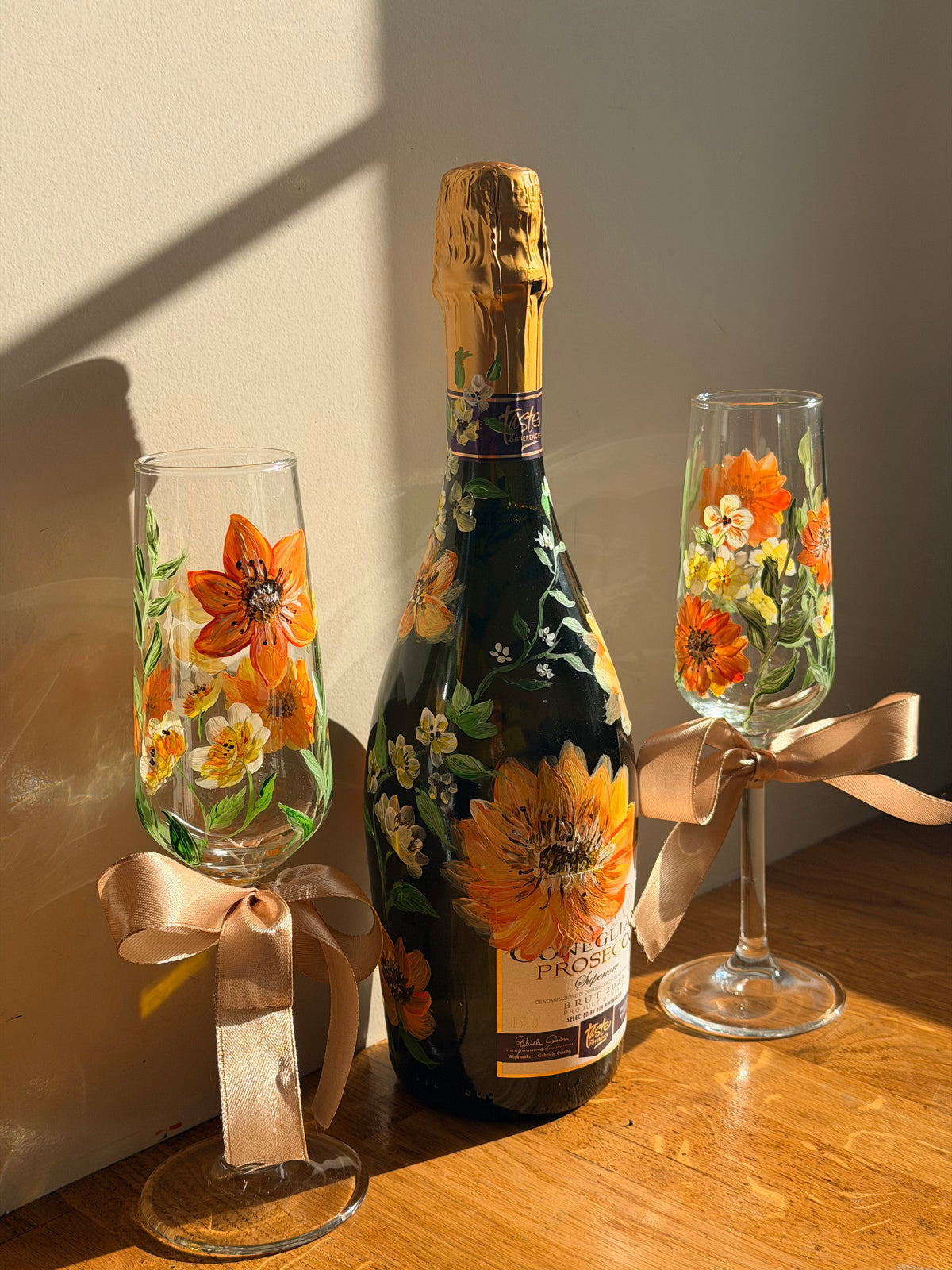 Hand-painted stemmed wine glasses with orange flower designs and satin bows