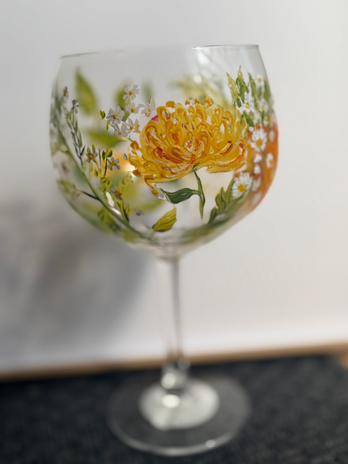 Hand-painted stemmed wine glass with orange flower and green leaves on clear glass