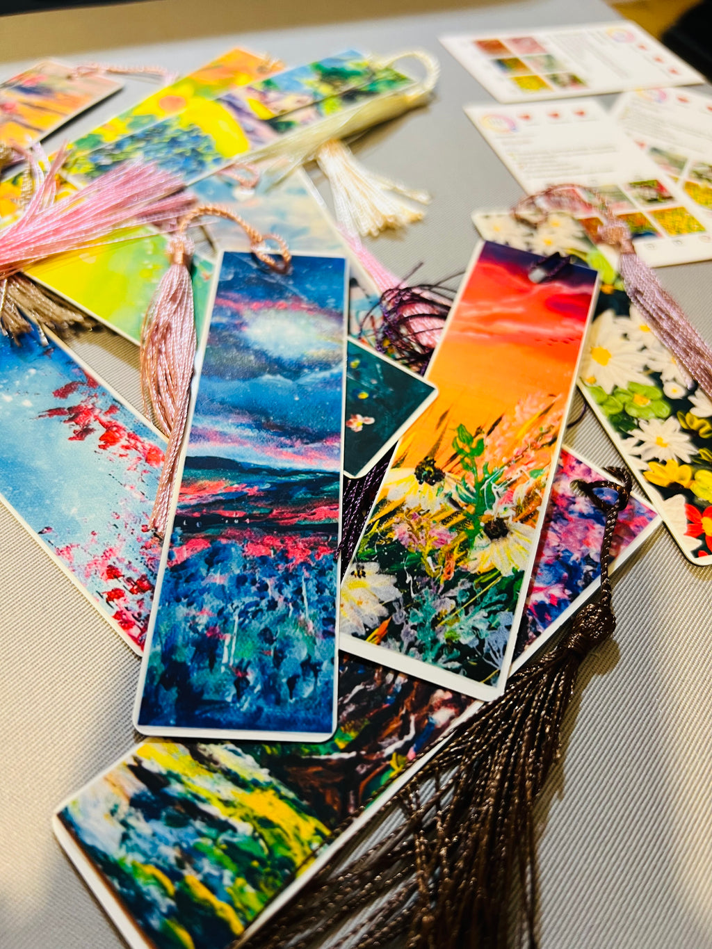 Metal bookmarks with vivid sky, garden, and sunset prints, each with tassels.