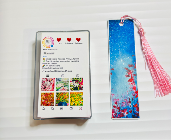 Metal bookmark with blue floral artwork and pink tassel string.