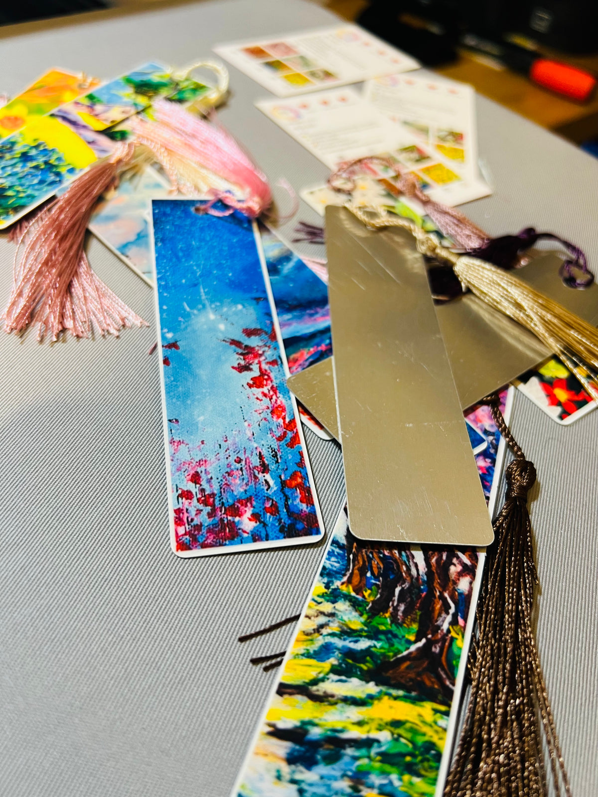 Metal bookmarks with bright landscape art prints and gold tassel accents.