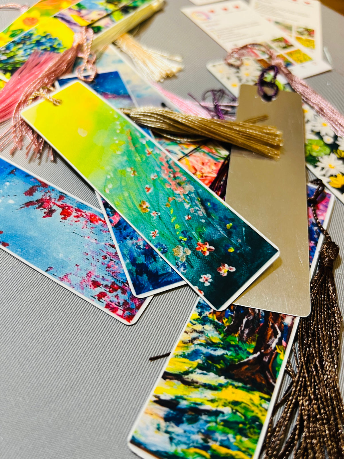 Metal bookmarks with multicolor floral and landscape art and tasseled ends.