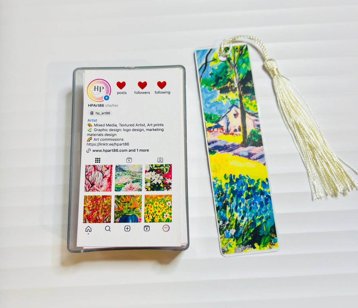 Metal bookmark with green and blue landscape artwork and white tassel.