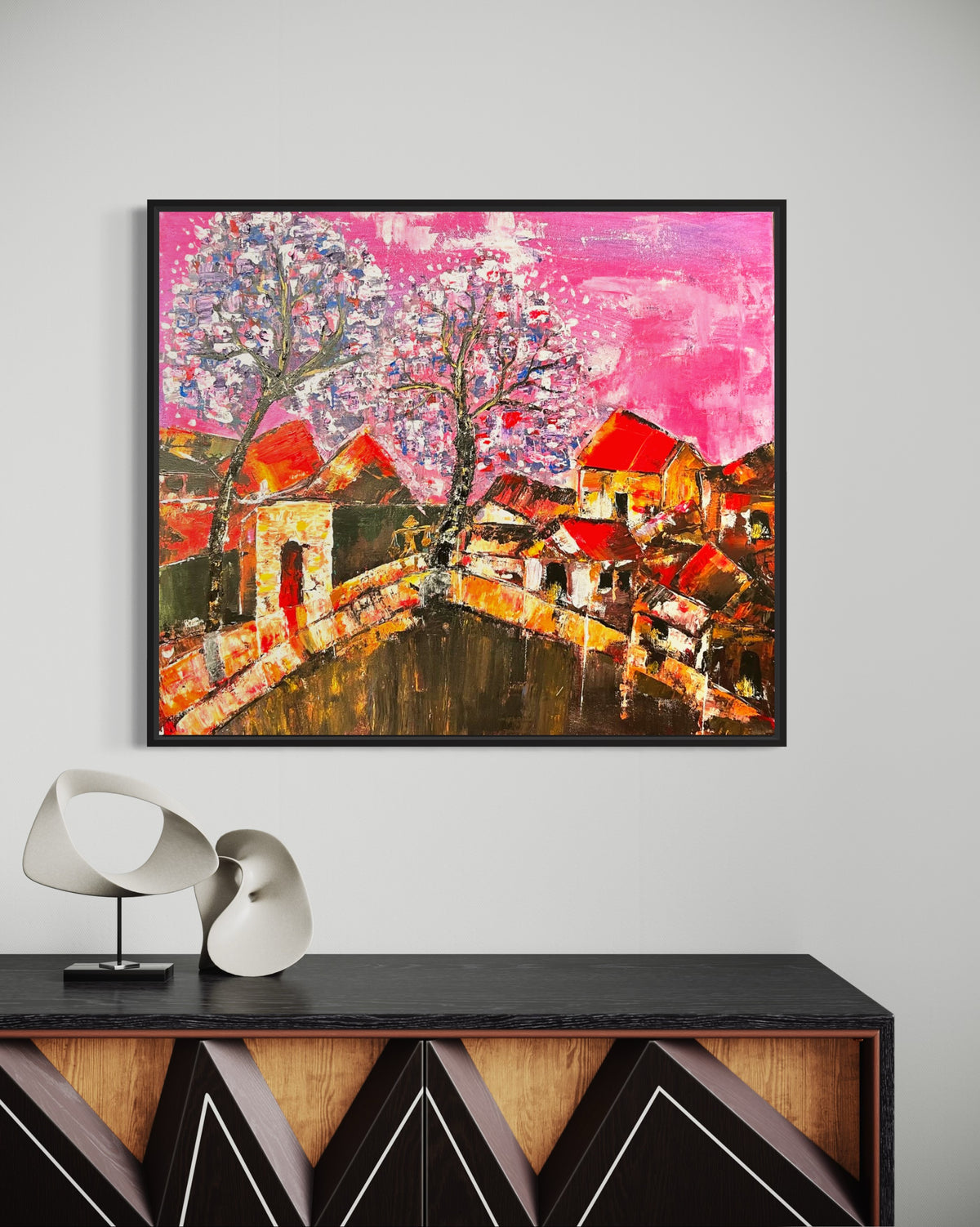 Square framed cityscape artwork with colorful houses, curved bridge, and bright pink abstract sky.