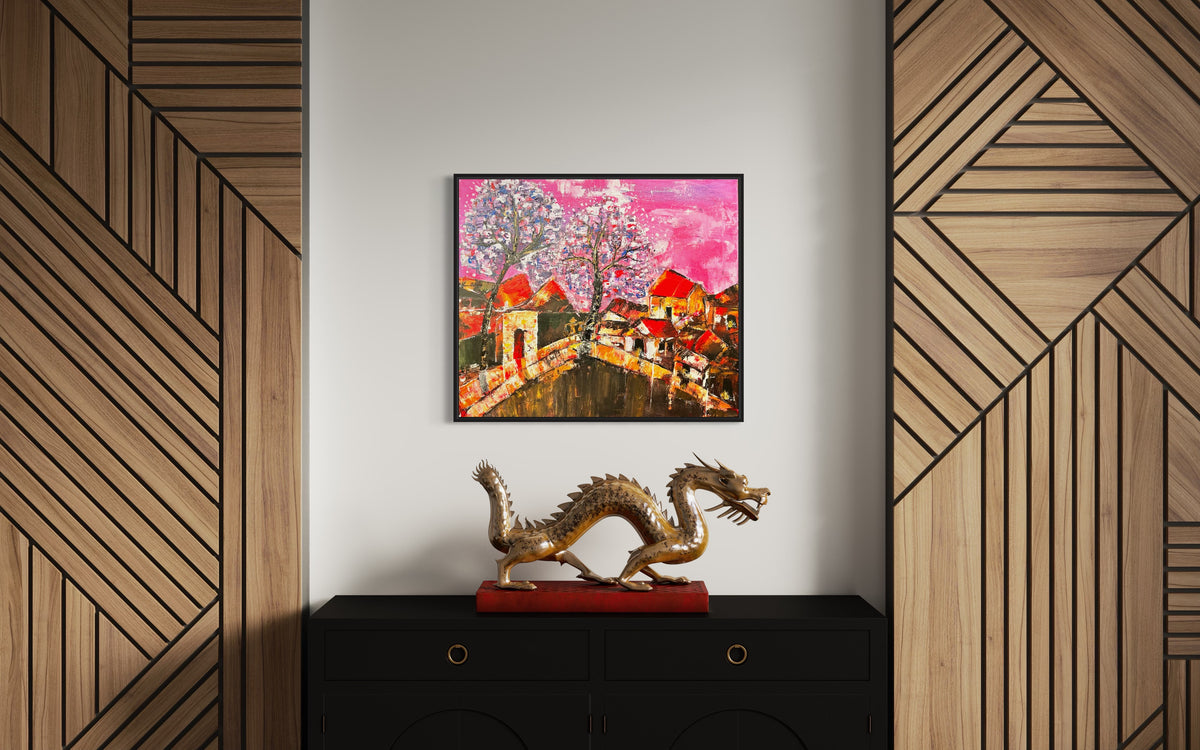 Framed small cityscape painting with orange roof houses, bridge path, and pink textured sky.