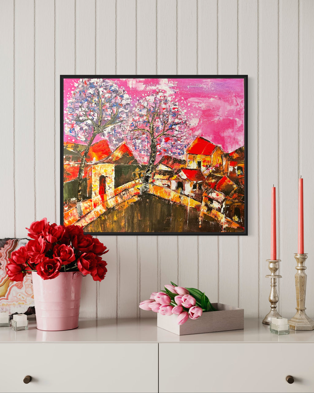 Framed cityscape artwork with orange houses, winding bridge, and pink splatter sky with a tree.