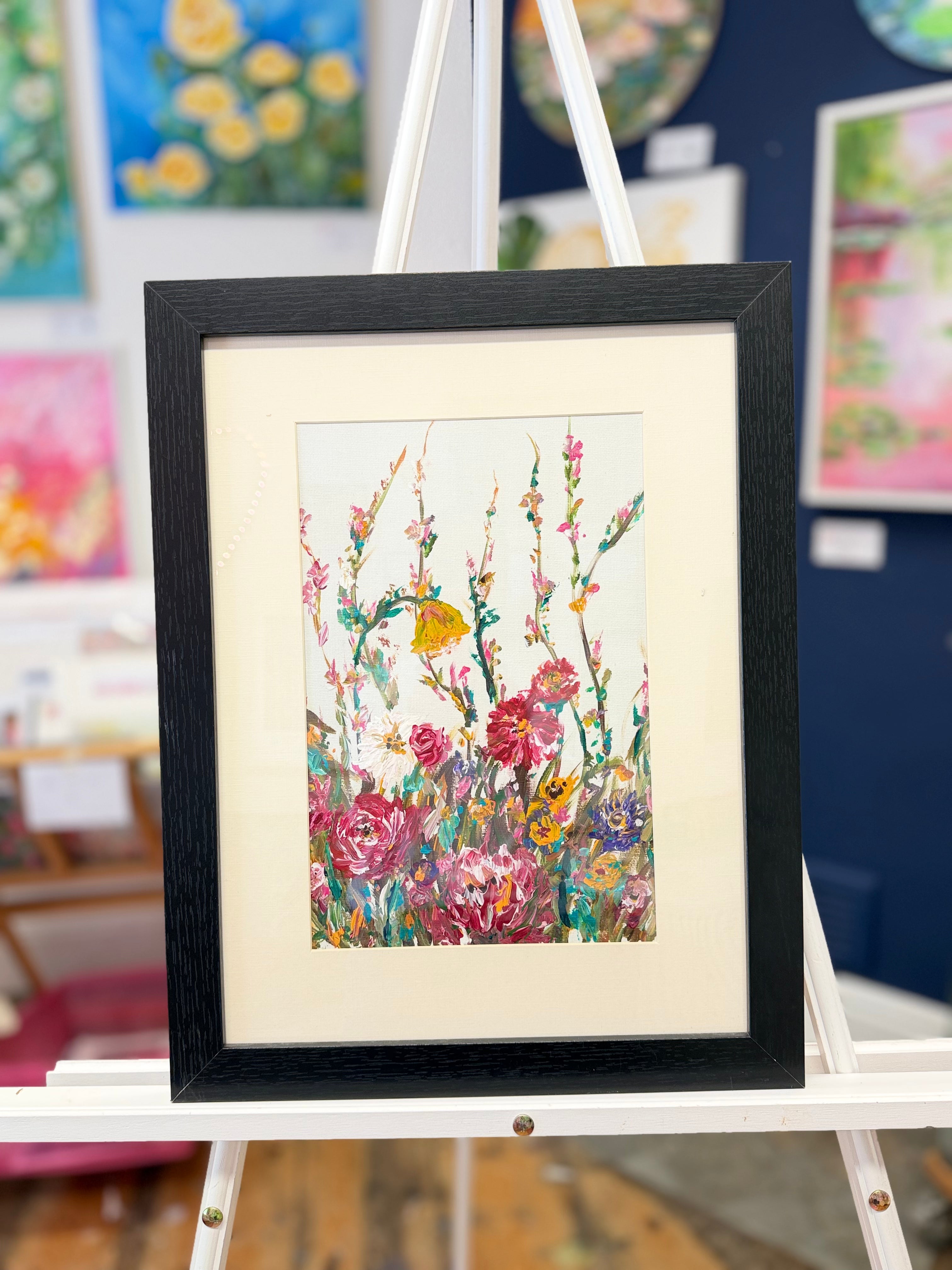Framed floral wall art print with colorful flowers and green stems in a black frame