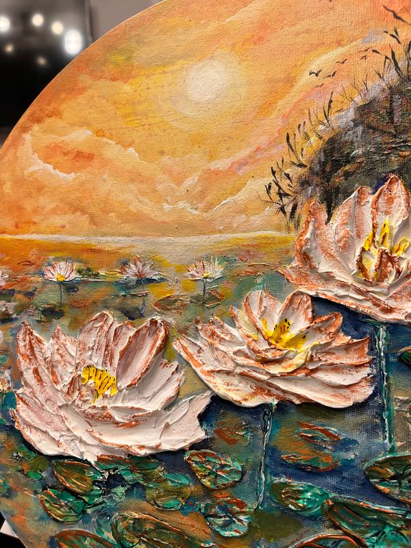 Round canvas wall art showing waterlily pond with white blossoms, orange sky, and dark shoreline reeds