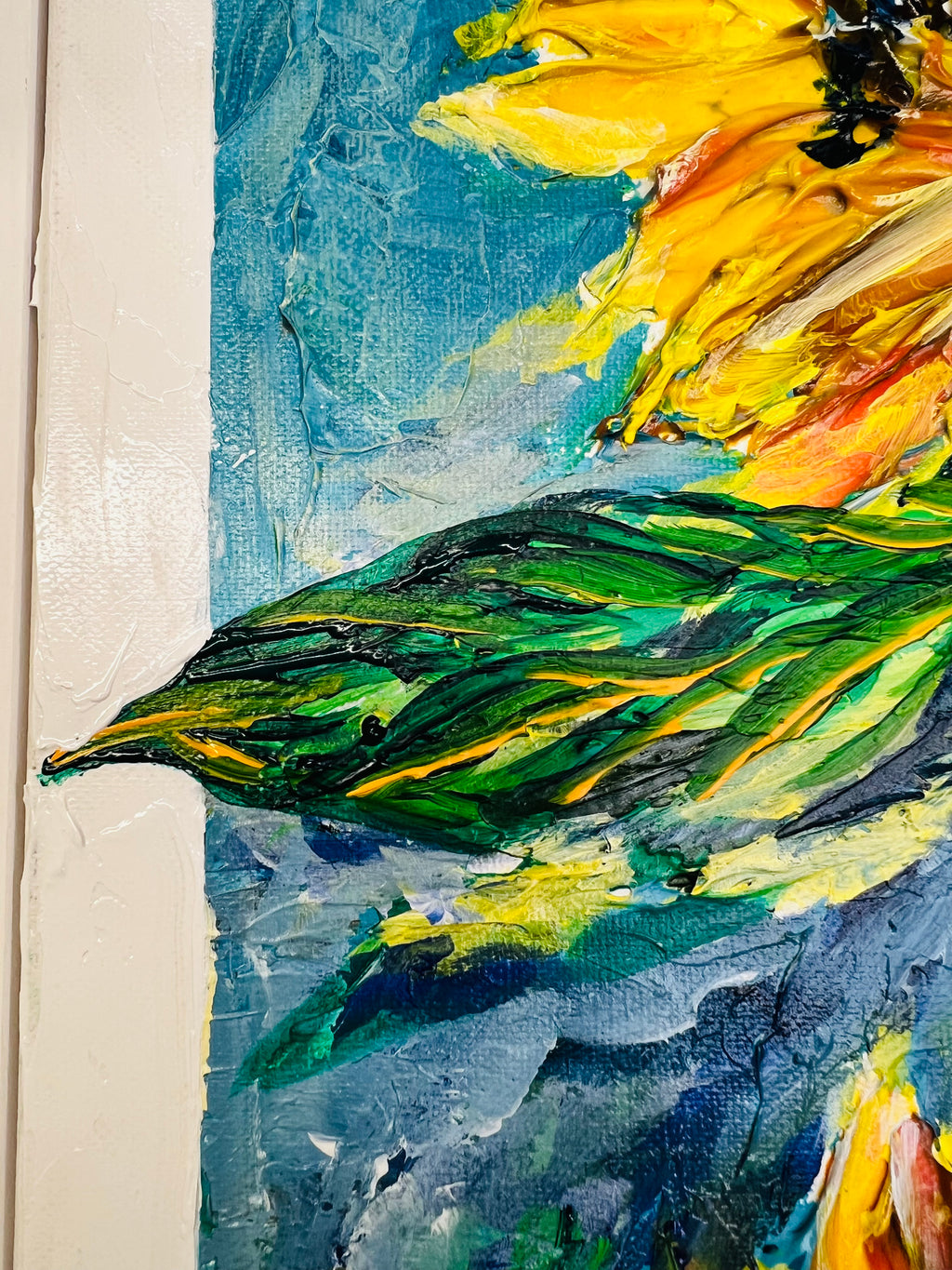 Close-up framed painting edge showing blue sky tones and green foliage with yellow highlights.