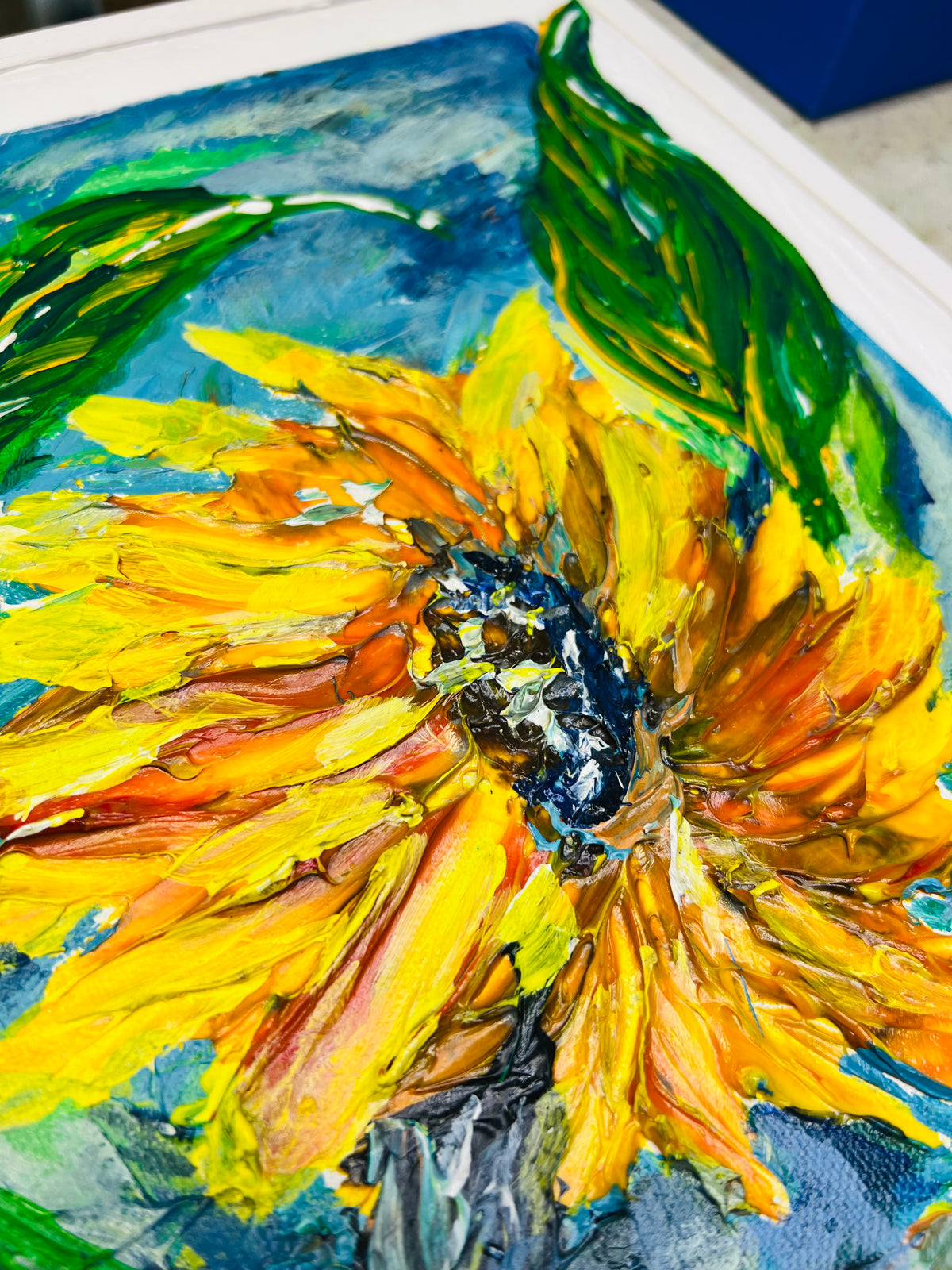 Framed sunflower painting close-up of a yellow bloom with textured green leaves.