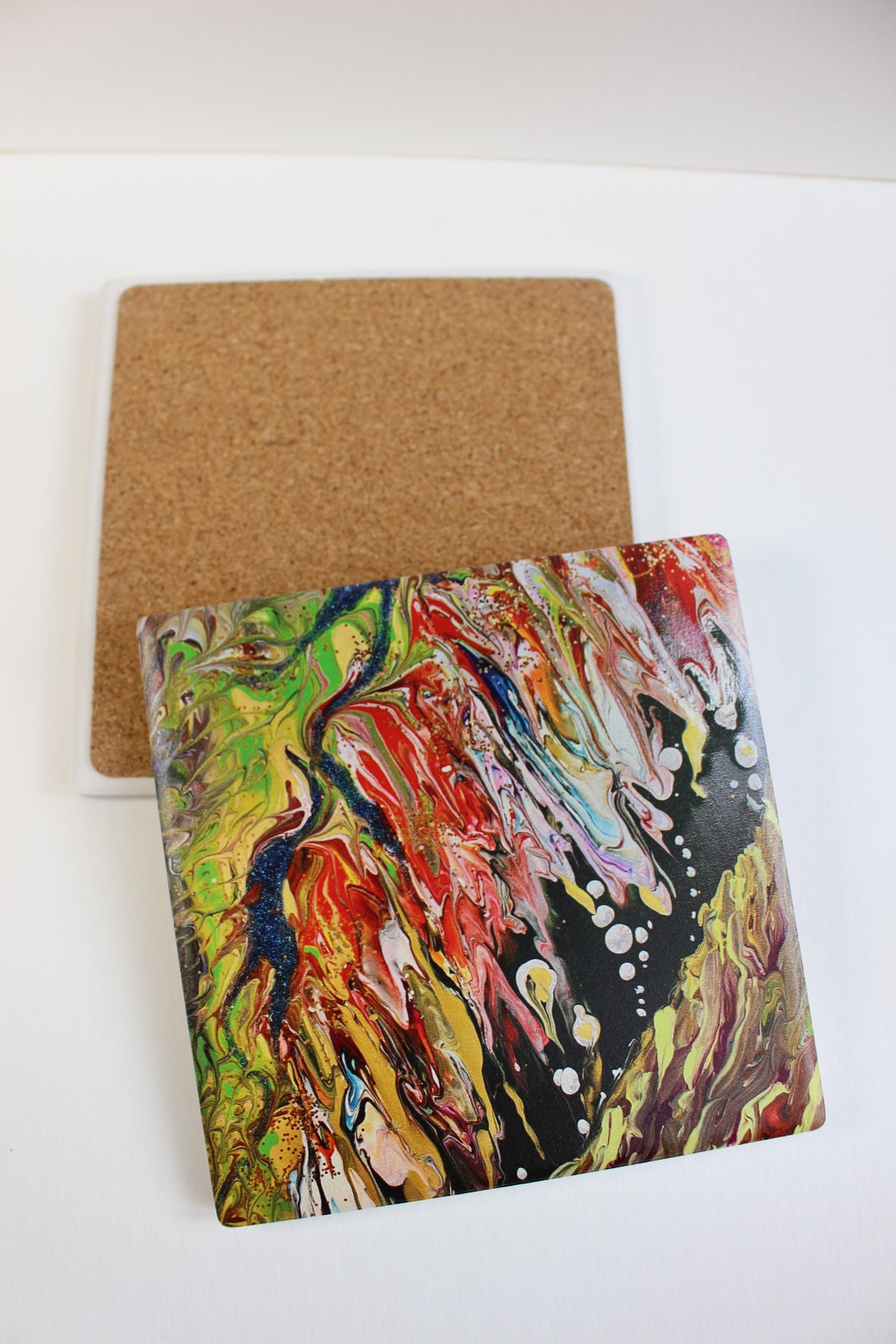 10x10cm square ceramic coaster featuring vibrant, hand-painted abstract art with a protective cork backing on a white surface.
