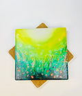 10x10cm square ceramic coaster featuring a vibrant green field art print with colorful wildflowers and a protective cork backing.