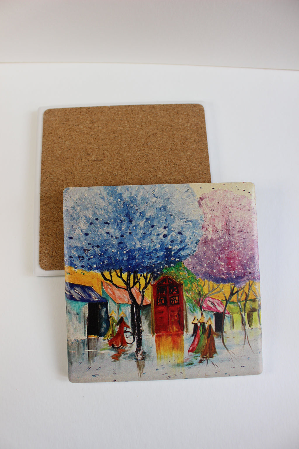 10x10cm square ceramic coaster with cork backing, featuring a colorful hand-painted Hanoi street scene with trees and figures.