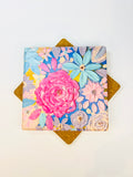 Square ceramic coaster with colorful floral design and pink rose, viewed from above