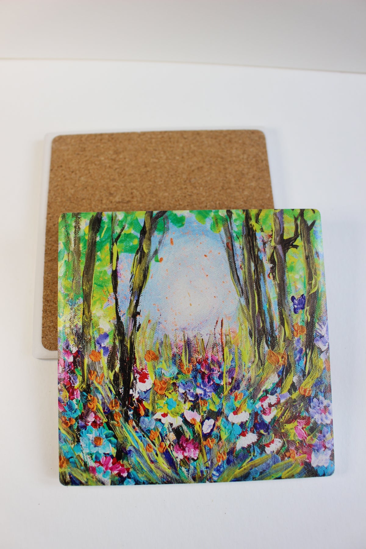 10x10cm square ceramic coaster featuring a colorful hand-painted floral forest scene with a protective cork backing.