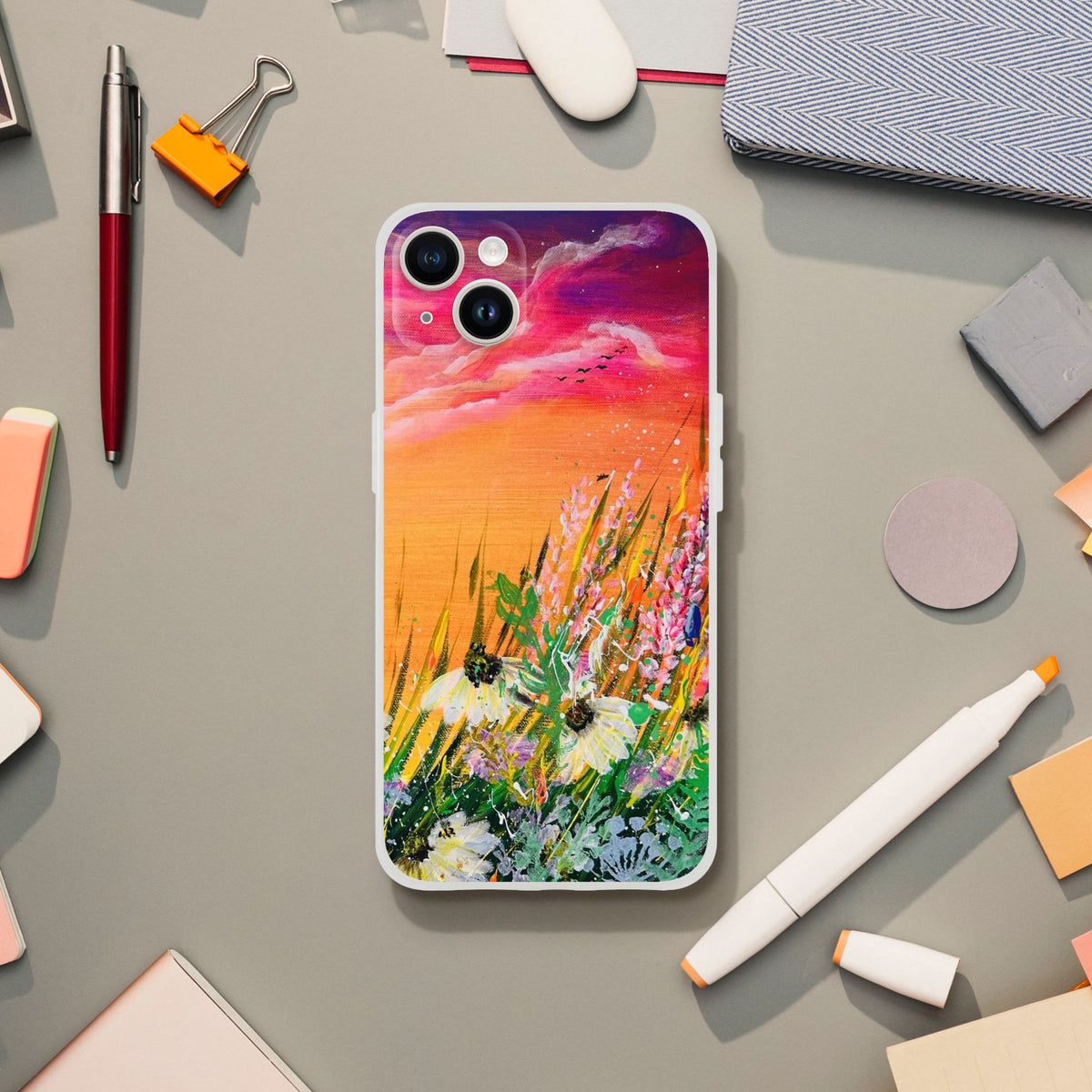 Flexible phone case featuring a vibrant sunset landscape painting with wildflowers on a desk with stationery.