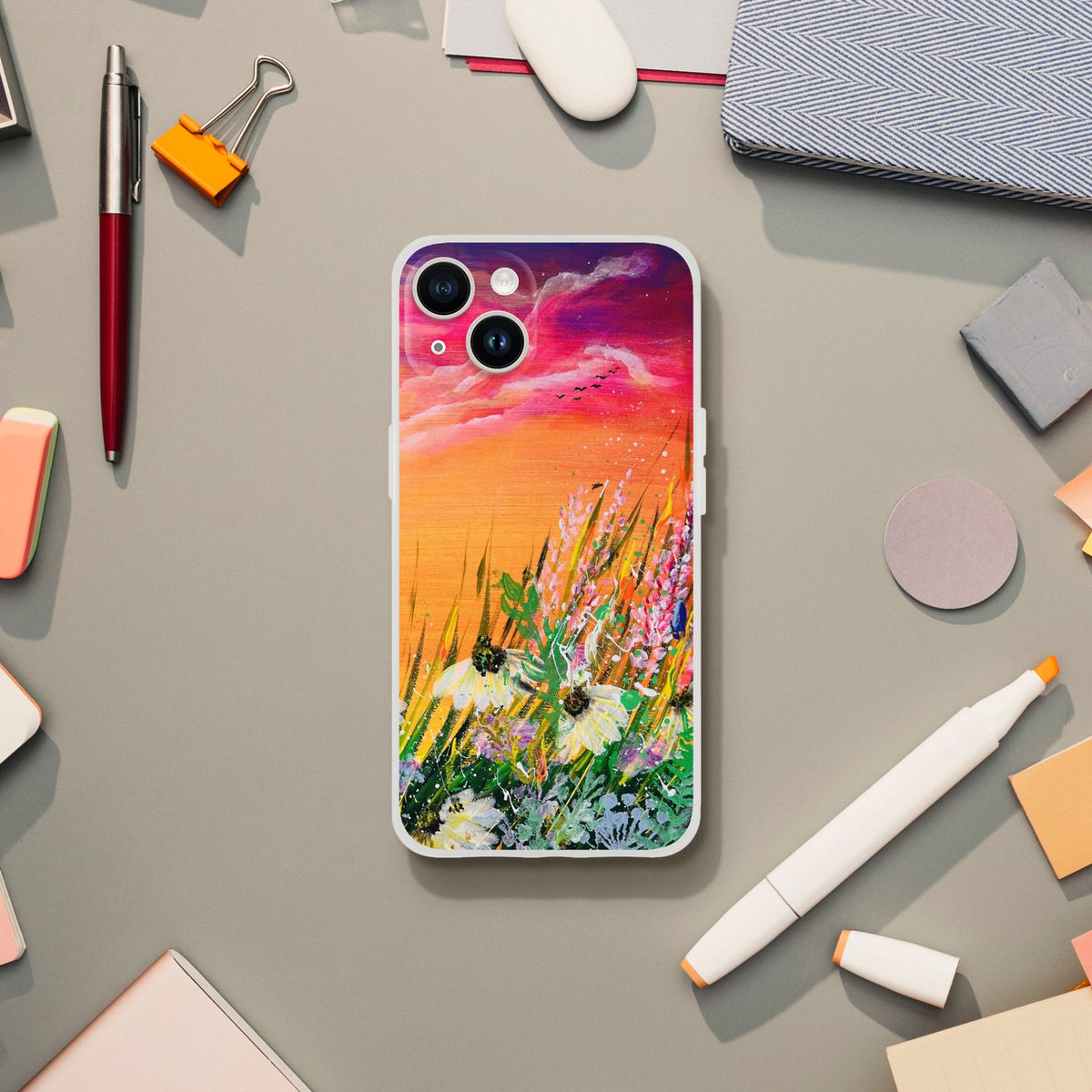 Flexible phone case featuring a vibrant sunset landscape painting with wildflowers on a desk with stationery.