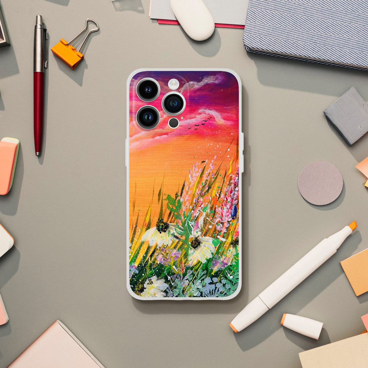 Flexible phone case featuring a vibrant, artistic sunset meadow painting with colorful wildflowers on a desk.