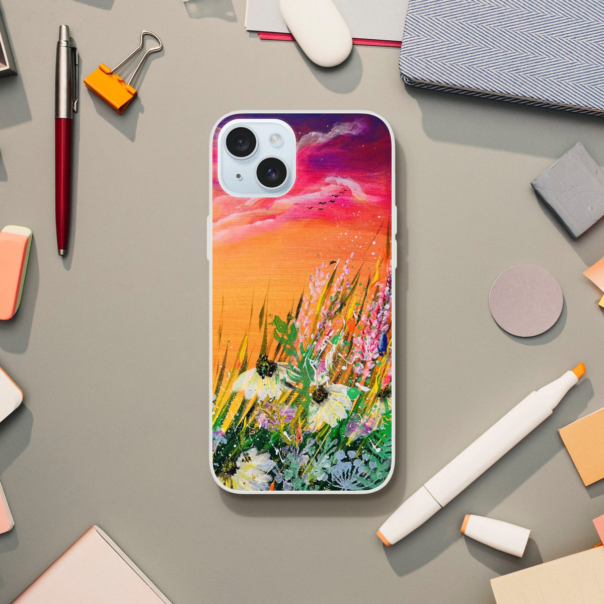 Flexible phone case featuring a vibrant sunset landscape painting with wildflowers on a desk with stationery.