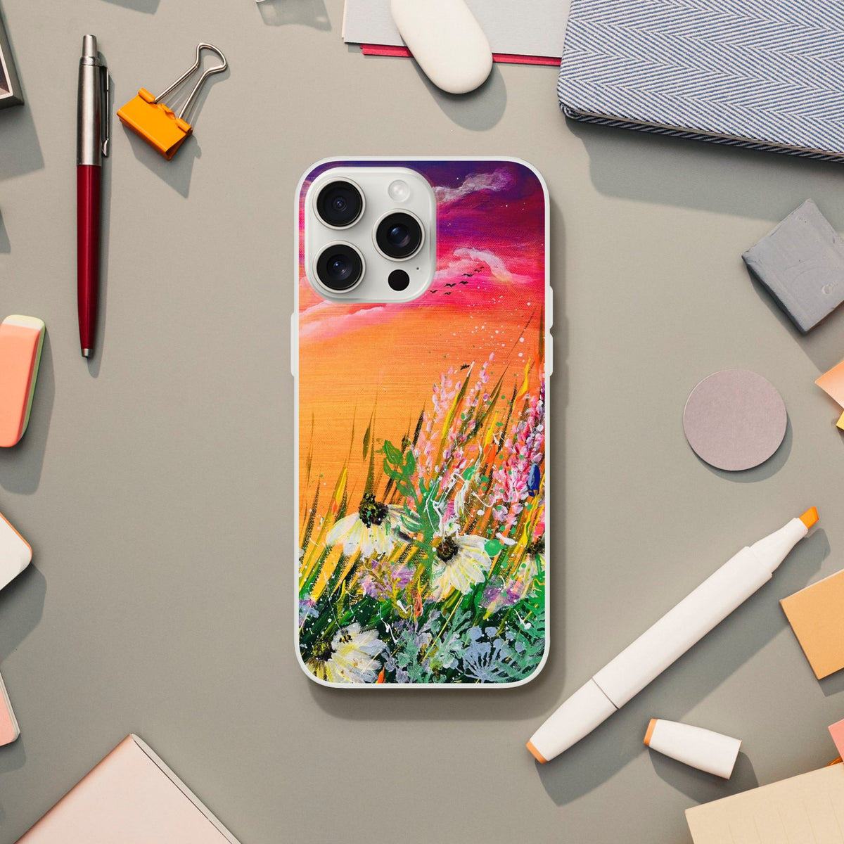Flexible phone case featuring a vibrant, colorful nature painting of wildflowers under a sunset sky on a desk.