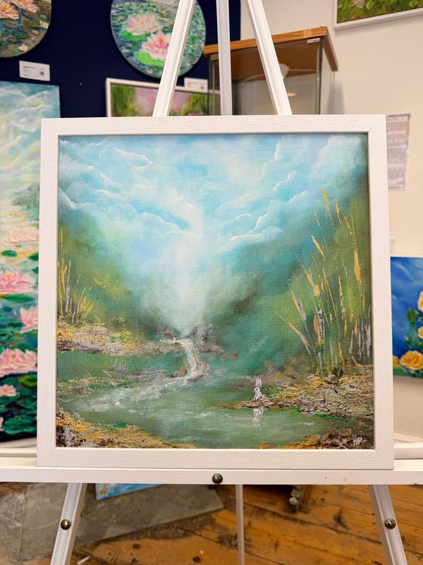 Framed acrylic landscape painting on easel with blue clouds, stream, and reeds
